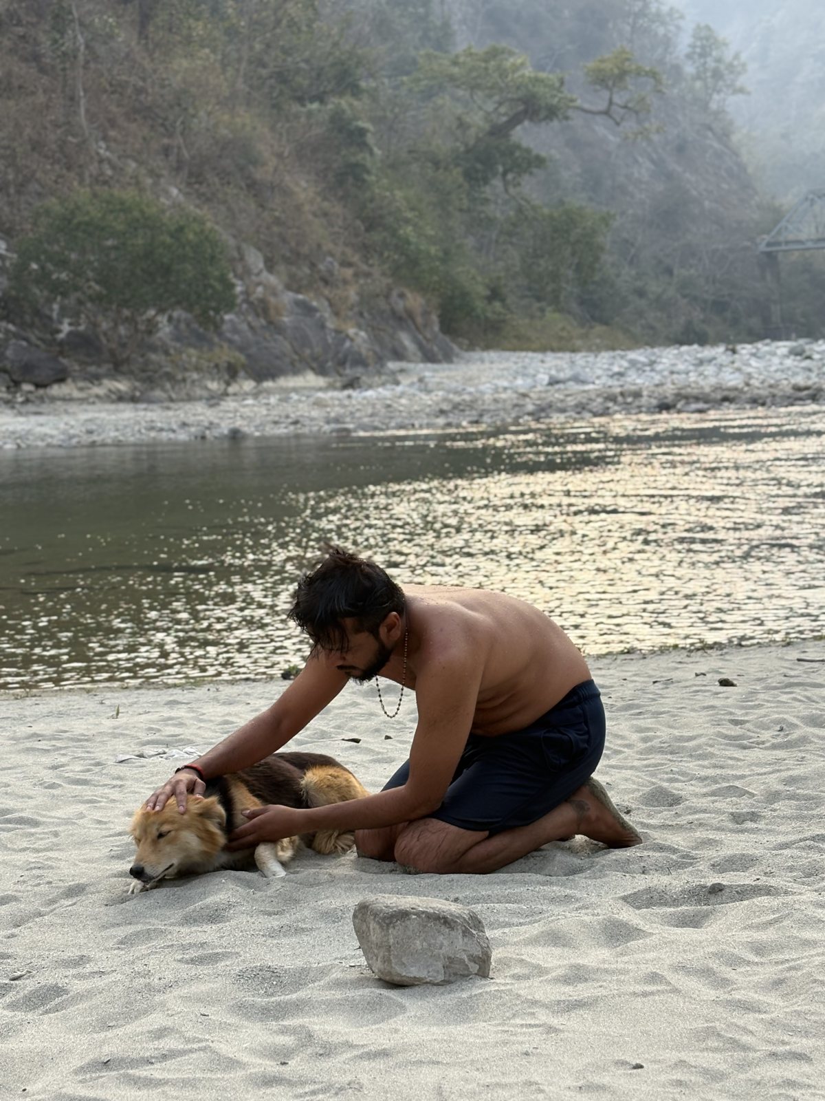 Pratik on a Himalayan riverbank comforting a resting dog