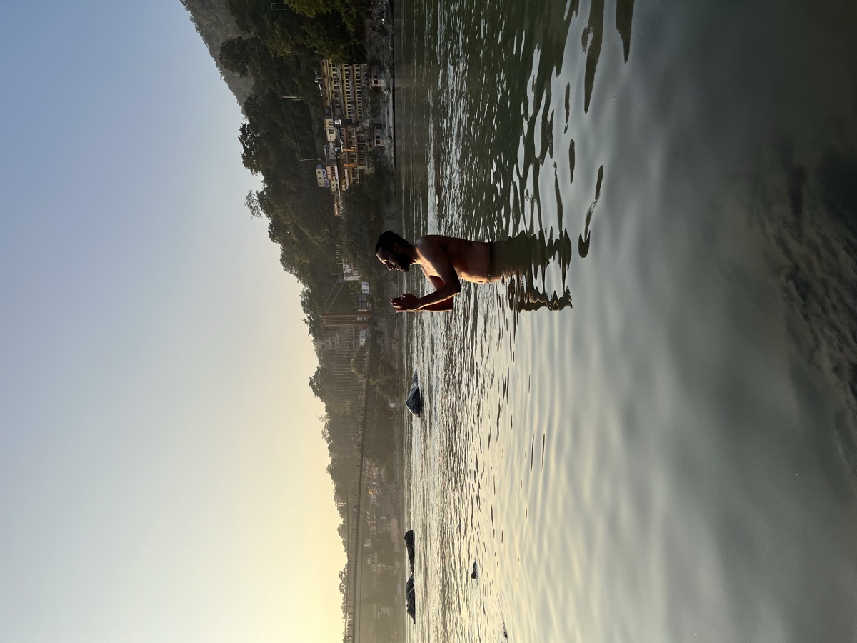 Pratik standing in the river at dawn, palms joined, suspension bridge behind