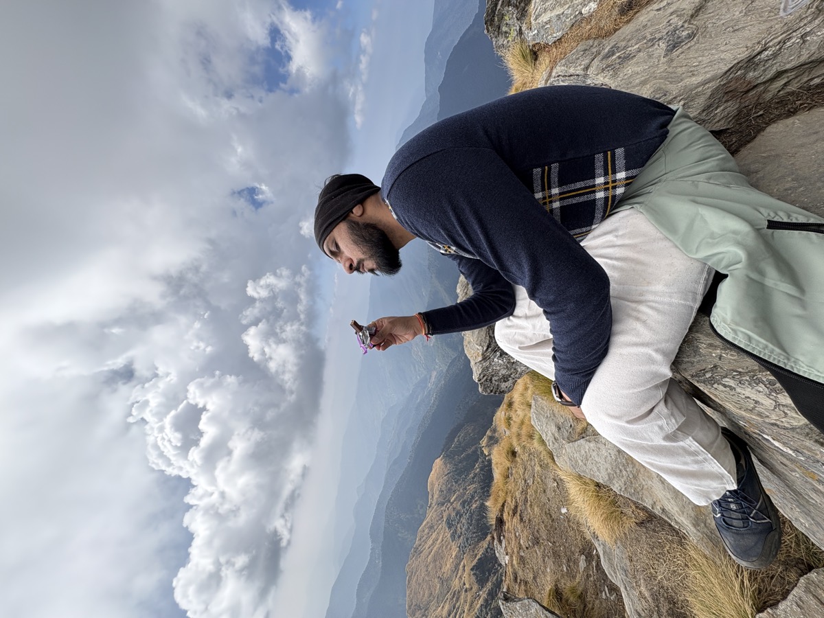 Pratik sitting on summit rocks eating chocolate above a sea of ridgelines